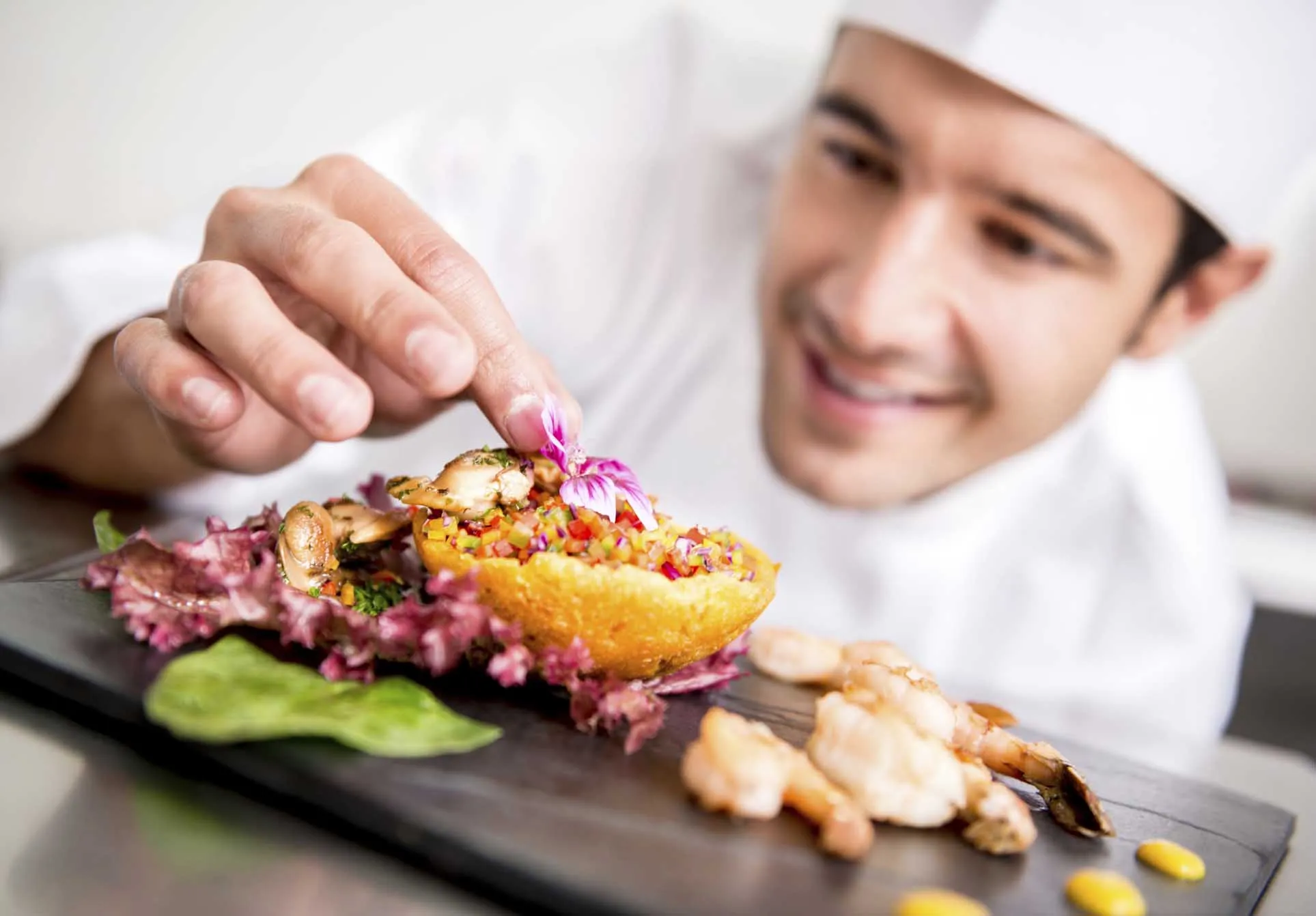 Chef garnishing a colorful dish with edible flowers, showcasing culinary artistry and attention to detail in restaurant food presentation.
