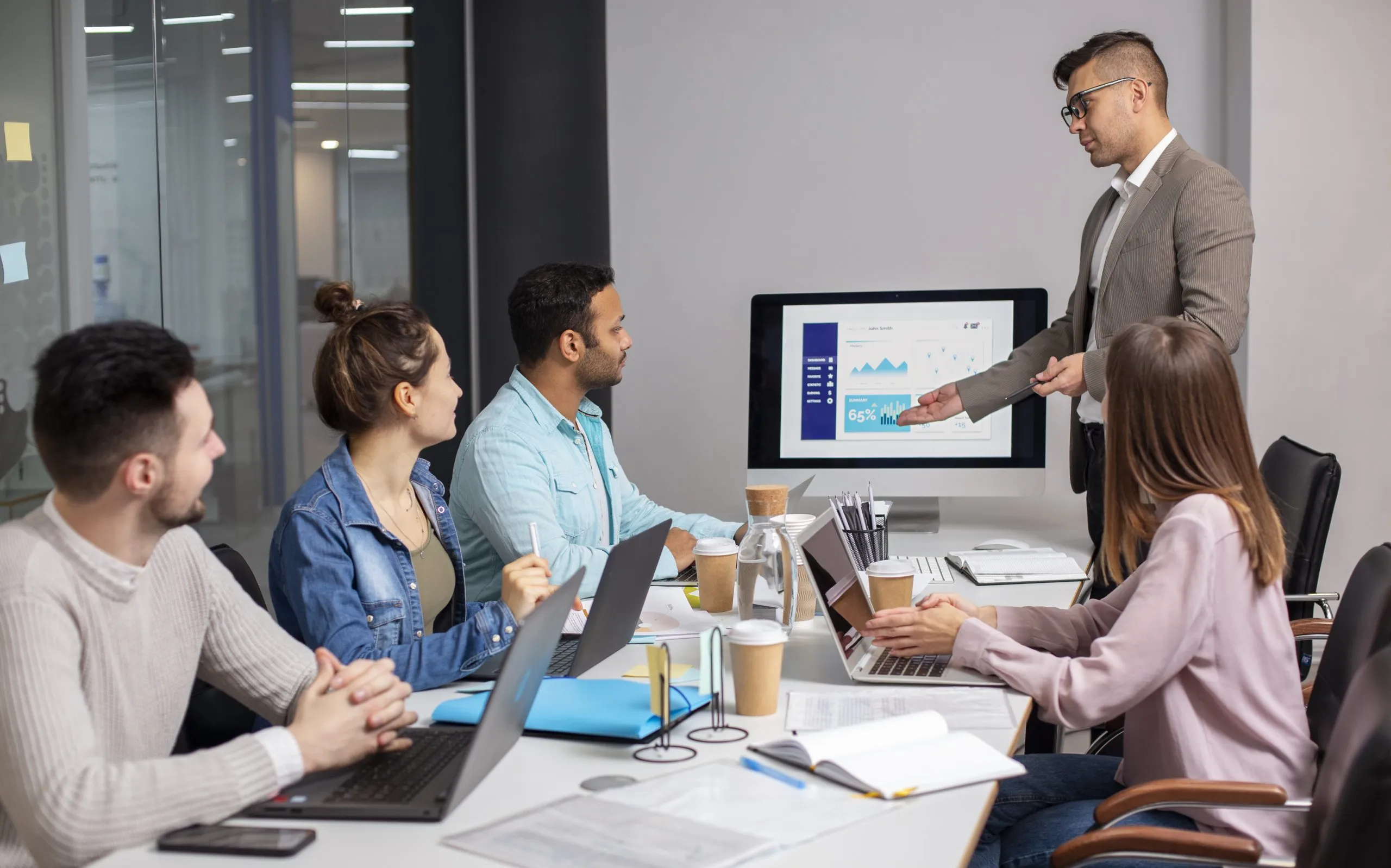 Team meeting in a modern office, discussing digital marketing strategies with a presentation displaying analytics and growth metrics on a screen.