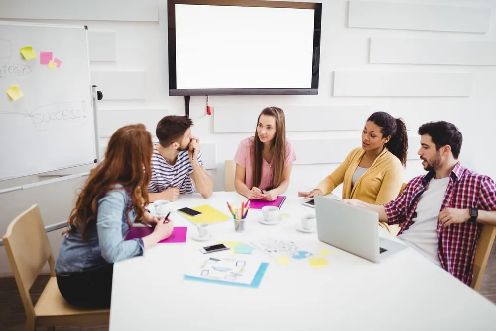 Group of young professionals discussing strategies in a modern meeting room, surrounded by digital solutions and collaborative tools, emphasizing teamwork and business growth.