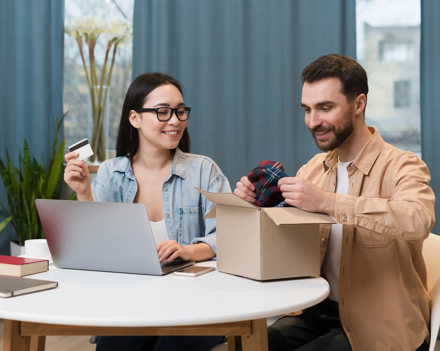Couple enjoying online shopping experience, woman holding credit card and man unpacking a box, showcasing ecommerce convenience and customer satisfaction.