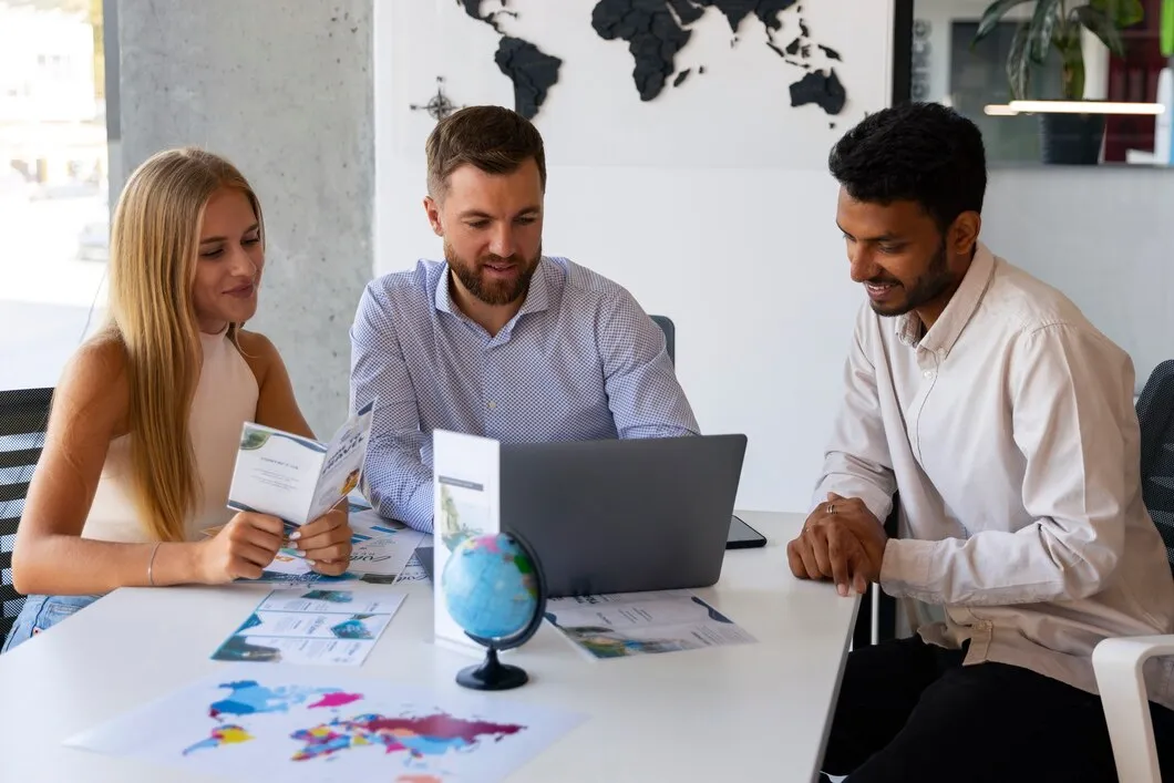 Three professionals collaborating at a table with a laptop, travel brochures, and a globe, discussing global SEO strategies for international audiences.
