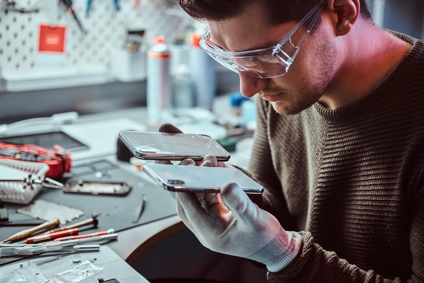 Electronic technician inspecting smartphone screens in a repair workshop, emphasizing app compliance and update management.