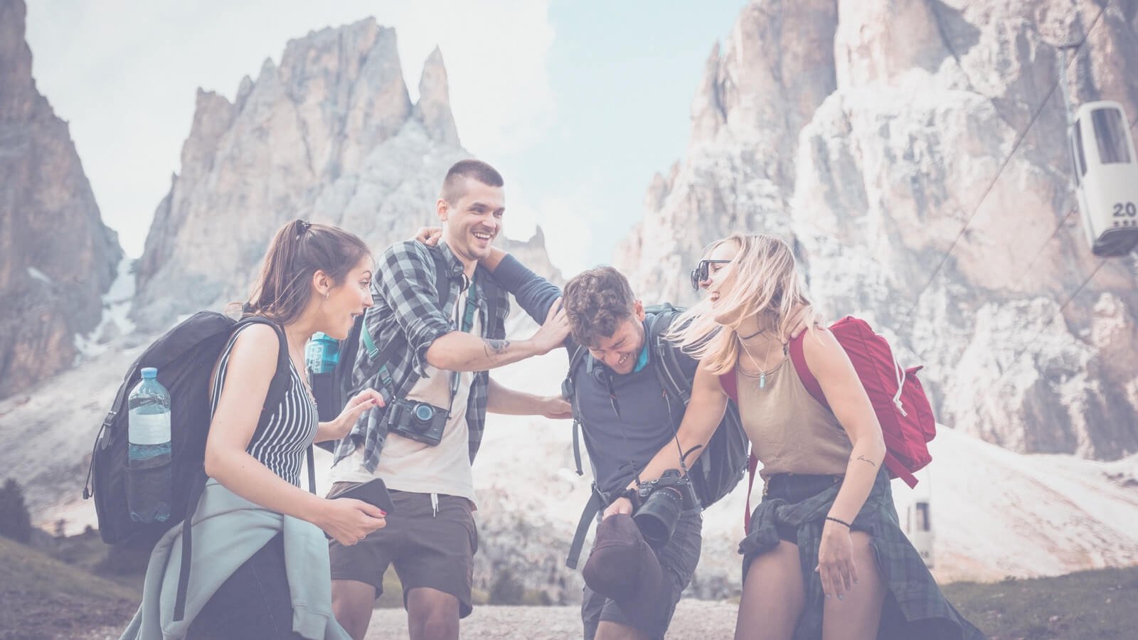 Group of friends laughing and enjoying a hike in the mountains, showcasing outdoor adventure and camaraderie, with backpacks and cameras, surrounded by rocky peaks.