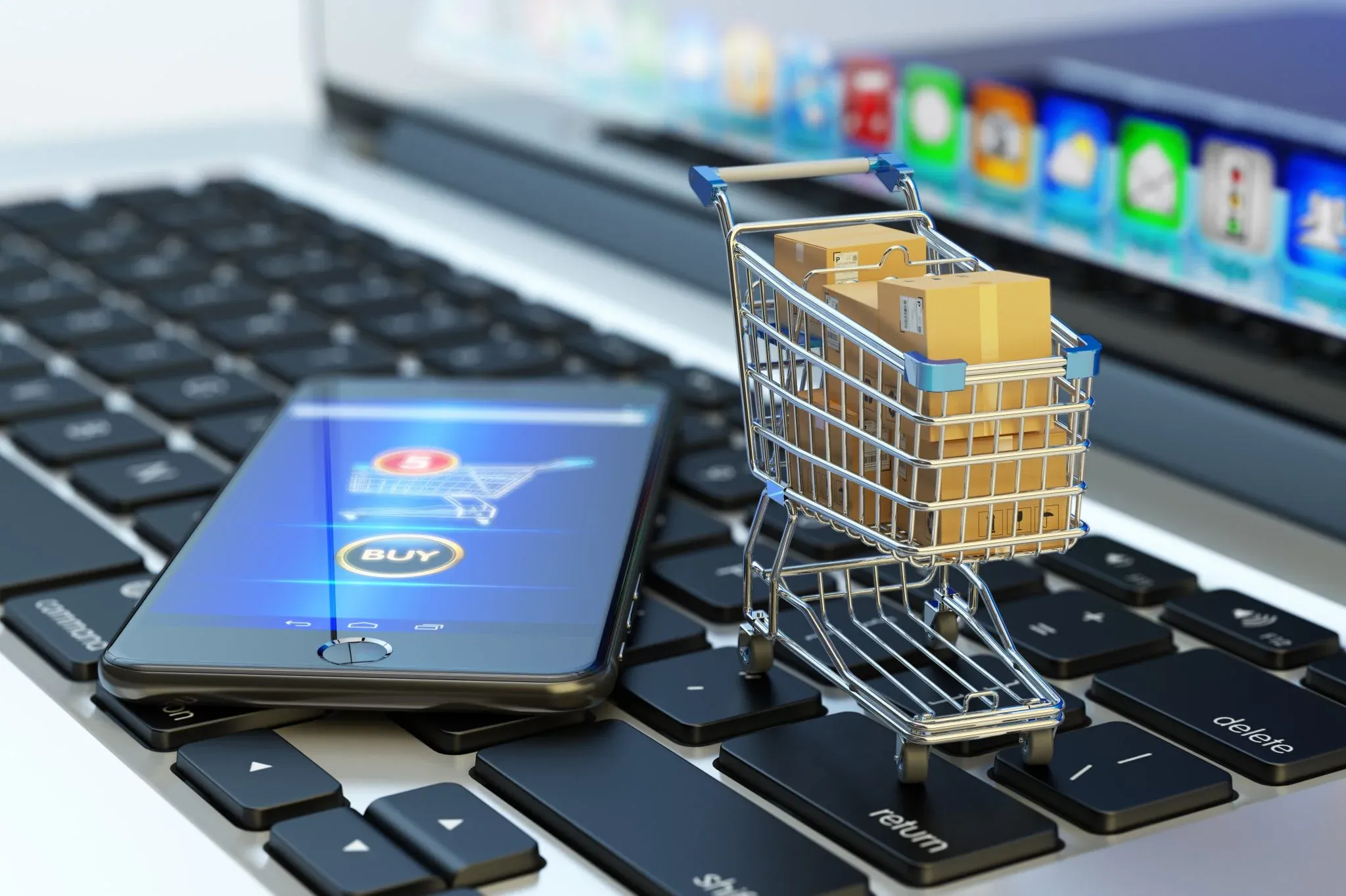 Mobile phone displaying eCommerce shopping interface next to miniature shopping cart filled with boxes on laptop keyboard, symbolizing seamless online shopping experience.