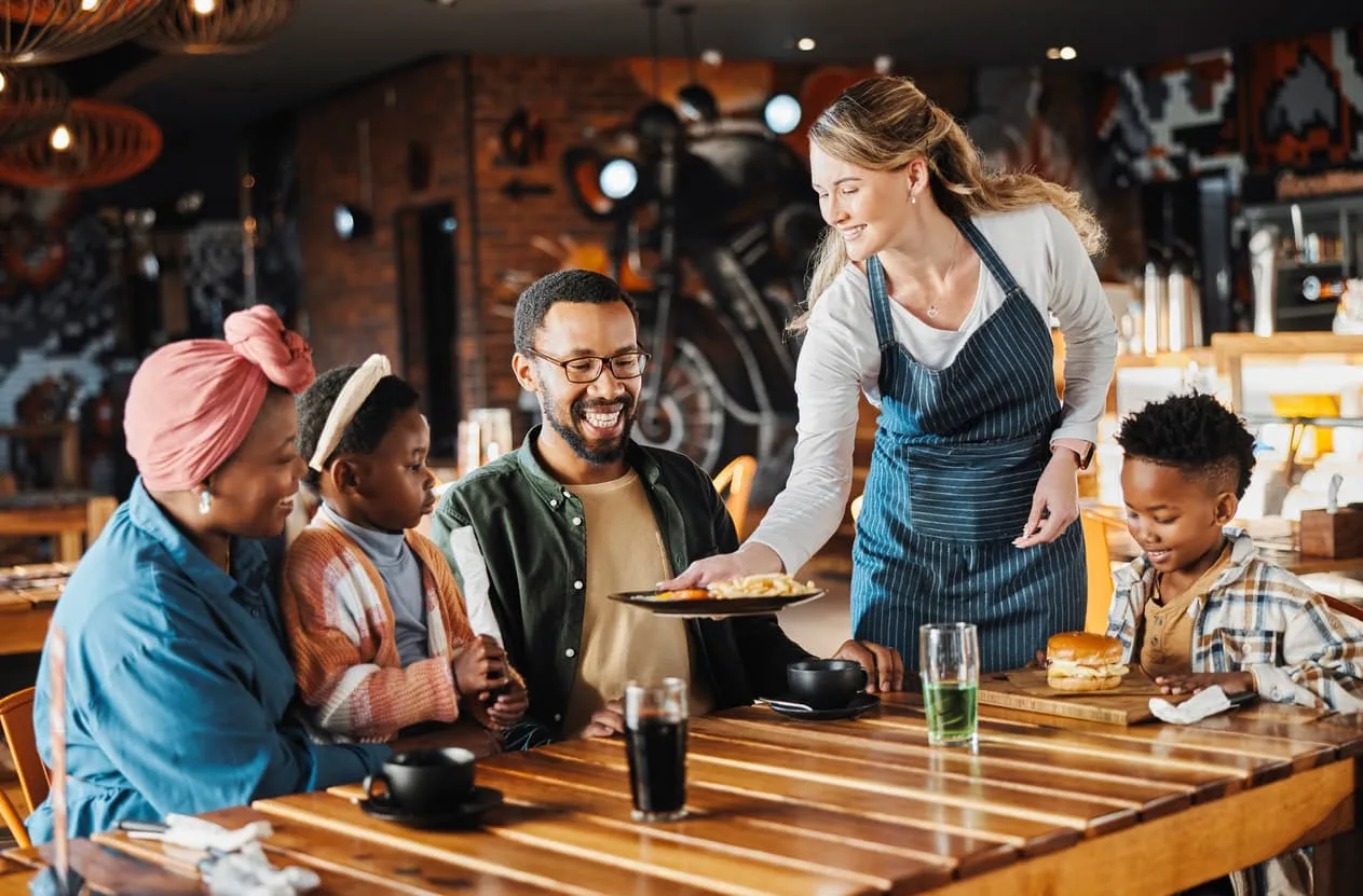 Family enjoying a meal in a restaurant, waitress serving food to smiling diners, emphasizing customer engagement and dining experience.