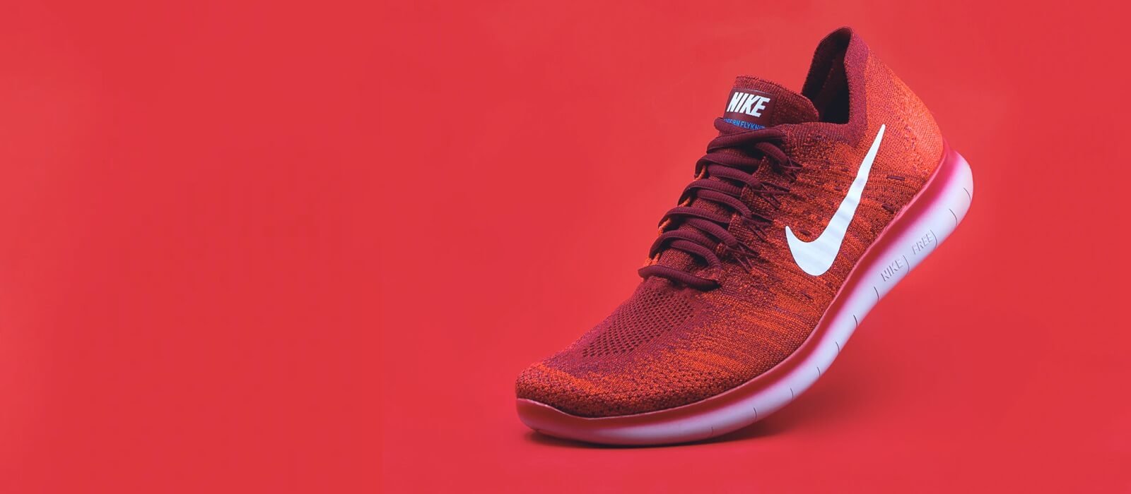 Nike Free running shoe in vibrant red and orange colorway against a solid red background, showcasing modern design and flexibility for active lifestyles.