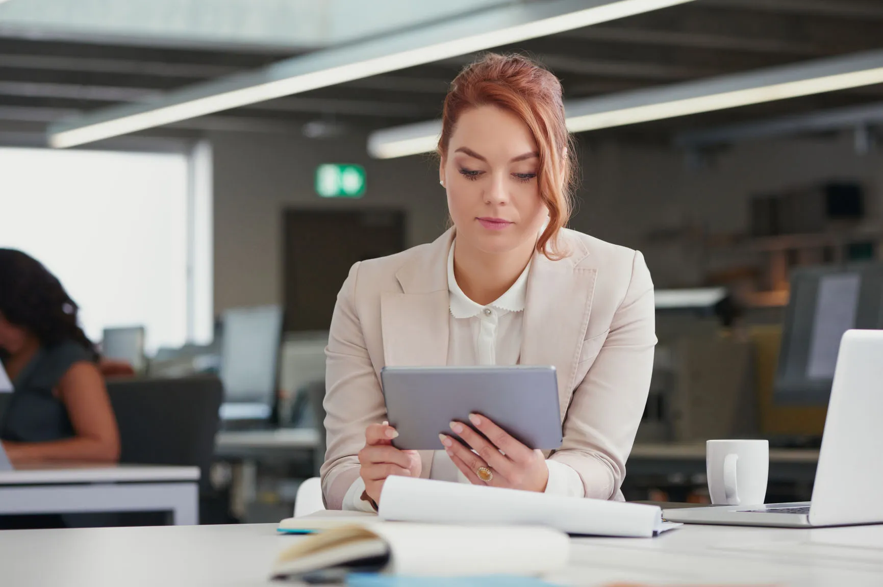 Professional woman in business attire using a tablet in a modern office setting, emphasizing digital engagement and productivity relevant to local SEO and Google Posts management.