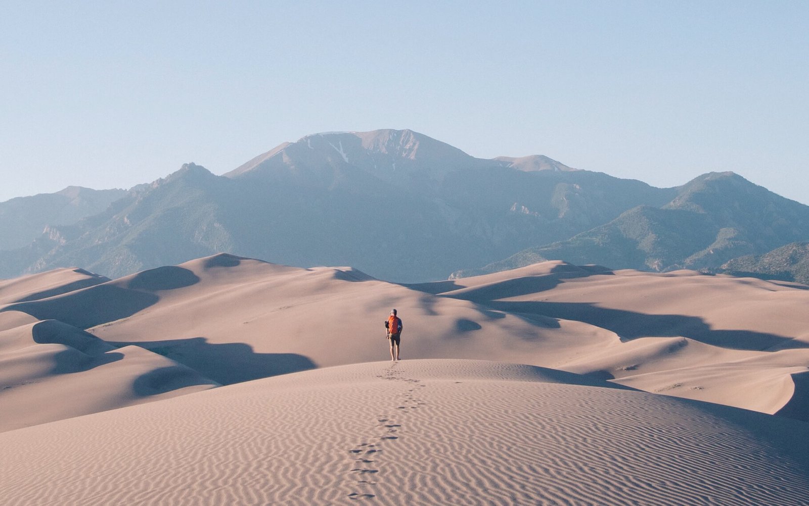 Person hiking through sand dunes with mountains in the background, illustrating outdoor adventure and exploration themes relevant to creative web design and digital solutions.